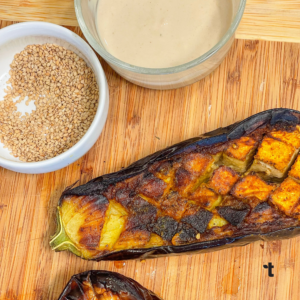 Roasted eggplant sits next to a bowl of uncooked fonio grains and tahini sauce.