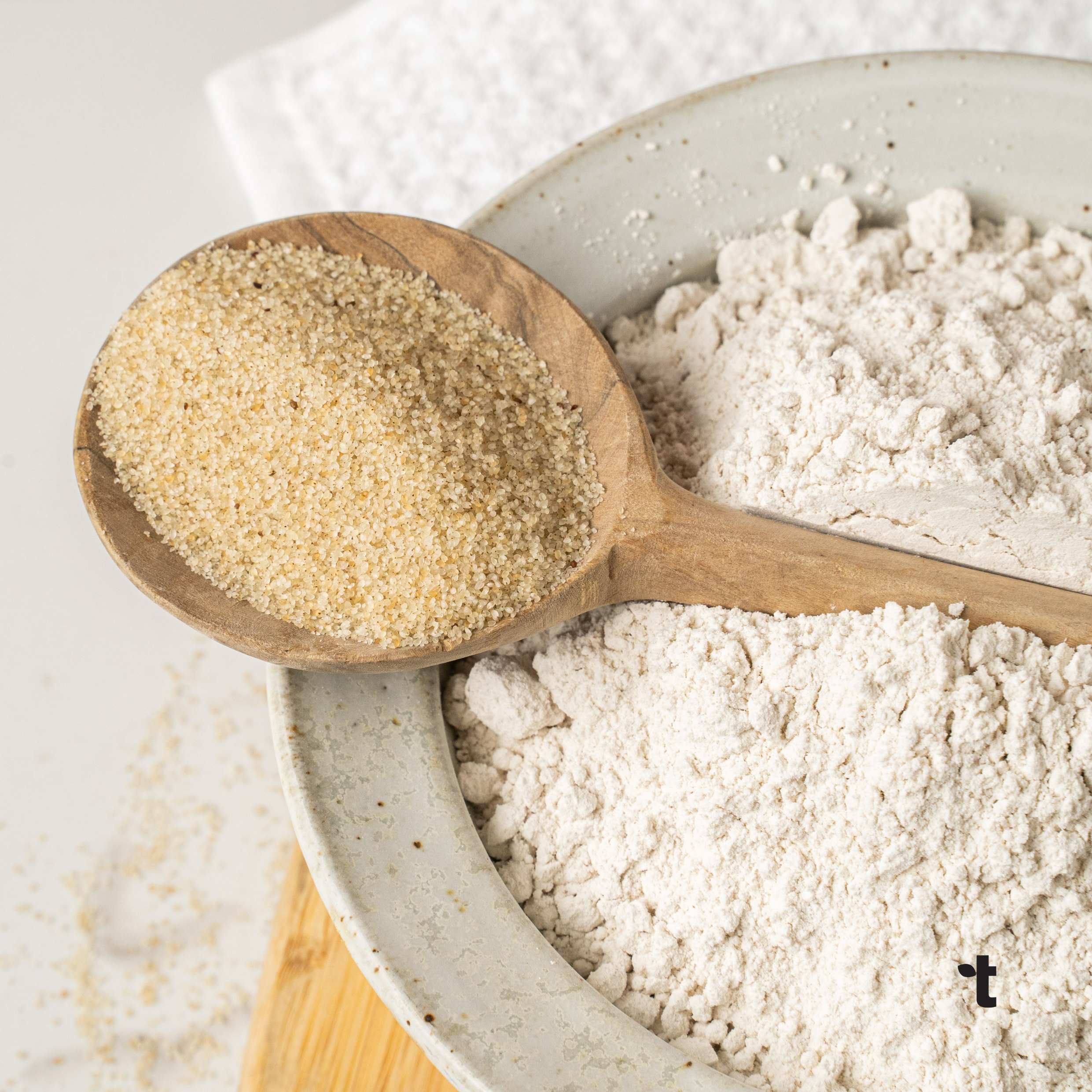 Fonio grain is displayed in a wooded spoon, resting on top of a bowl of fonio flour.