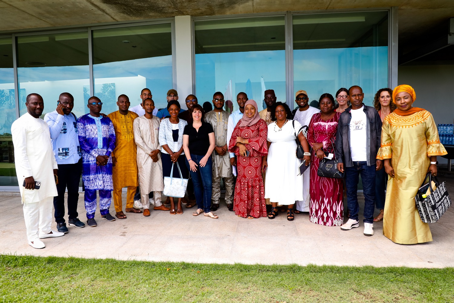 A group of men and women, many dressed in traditional African clothes, pose for a photo in front of a building.