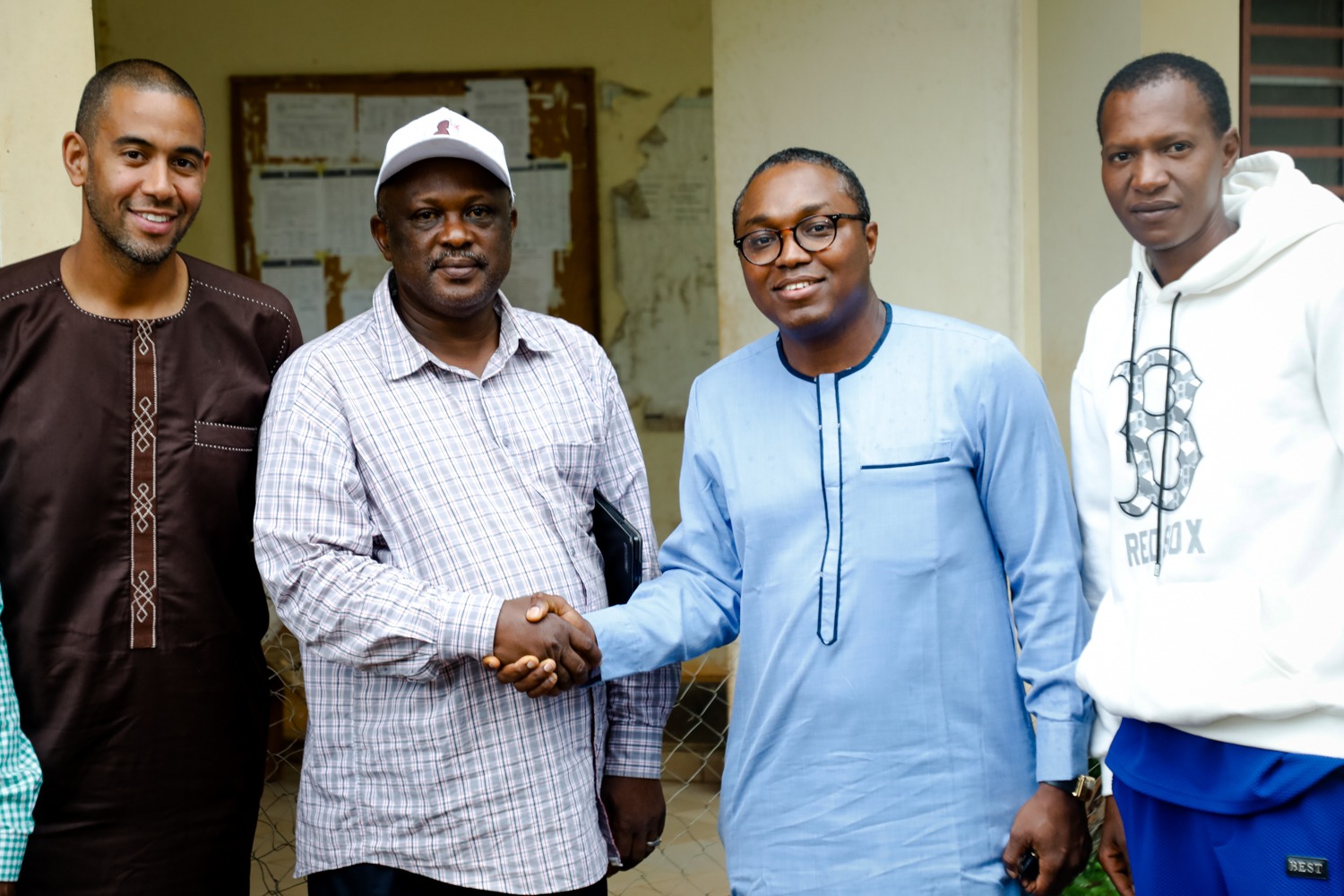 Two men shake hands in front of a government building in Koubia, Guinea