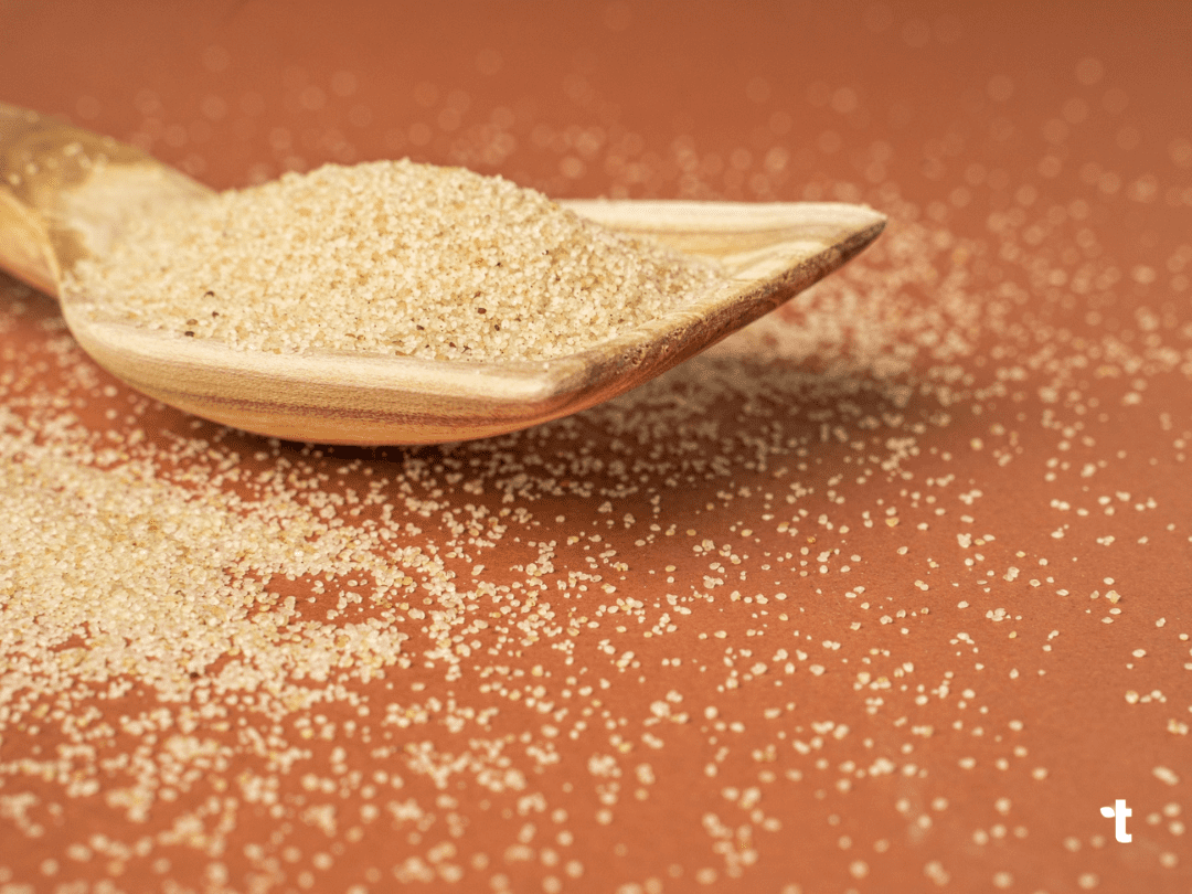 Uncooked fonio grain is scattered over a wooden spoon