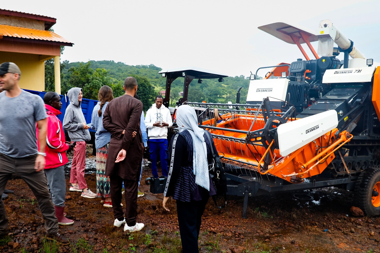 A group of men and women have a discussion in front of a large farming tractor on a muddy farm