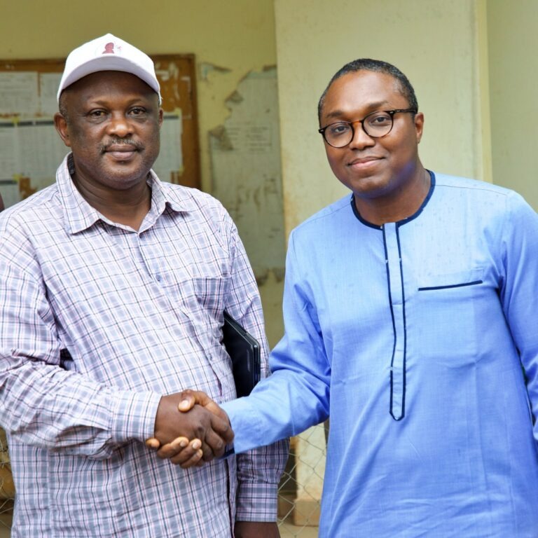 Two men shake hands while posing for a photo