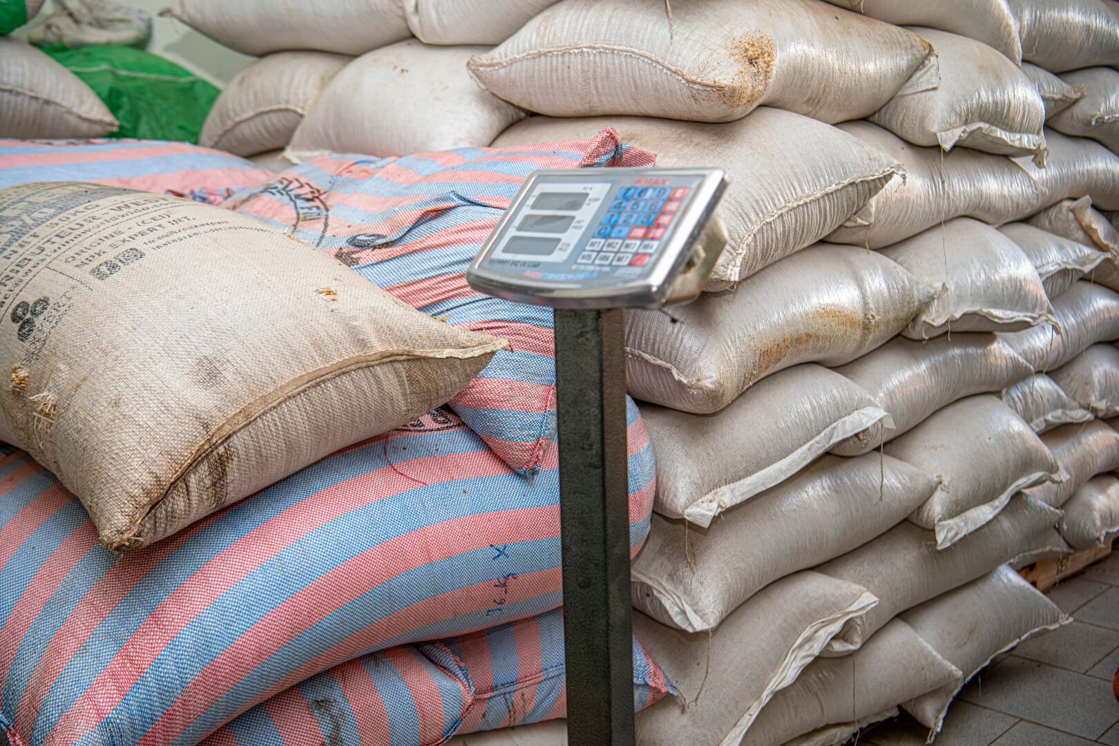 Bags of grain are stacked on top of one another next to a large weight scale